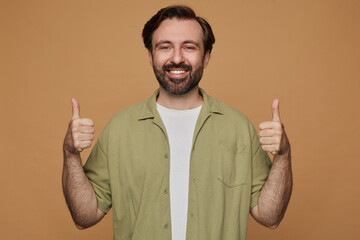 studio portrait of bearded man posing over beige background showing thumbs up sign