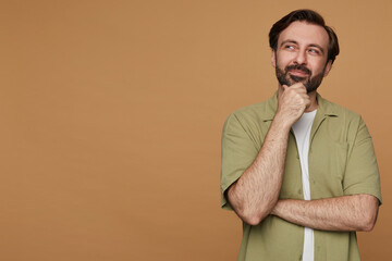 studio portrait of bearded man posing over beige background looking aside with broad smile on his face