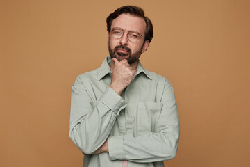 studio portrait of bearded man posing over beige background looking aside with serious facial expression