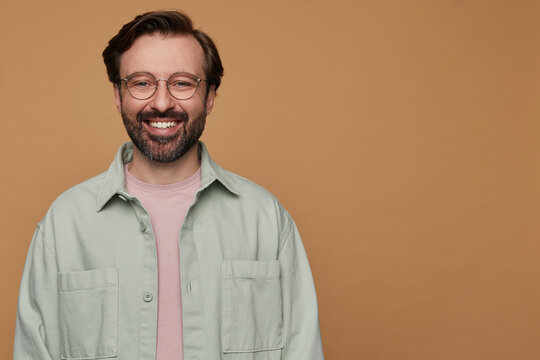 studio portrait of bearded man posing over beige background looking into camera with broad smile on his face