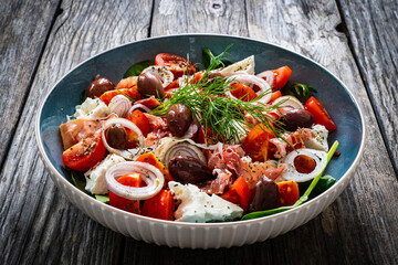 Tasty salad - prosciutto di Parma, feta cheese, cherry tomatoes, black olives and fresh, green vegetables on wooden table 