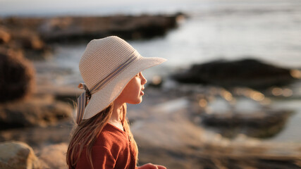 Cute European teenage girl in hat and dress on the rocks on an empty seashore, © natalialeb