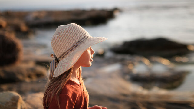 Cute European teenage girl in hat and dress on the rocks on an empty seashore,