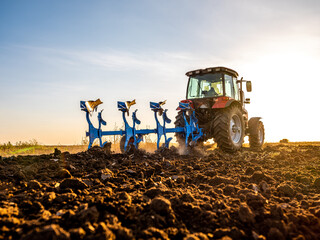 Farmer in tractor plowing preparing stubble field cultivating for seeding crops.