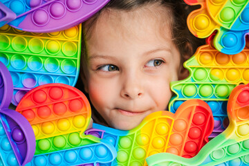 Fototapeta na wymiar Little girl,kid,child head among many,lots of colorful pop it. Children play. Trendy silicone antistress colorful sensory push toy popit. Flapping fidget. Rainbow color.Cure of autism.Stress reliever