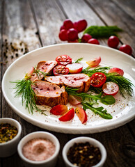 Roasted pork loin slices with dill and cherry tomatoes on wooden table