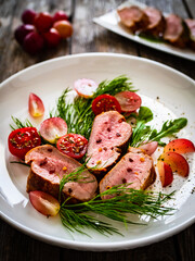 Roasted pork loin slices with dill and cherry tomatoes on wooden table