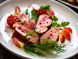 Roasted pork loin slices with dill and cherry tomatoes on wooden table