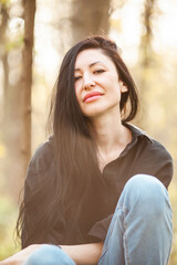 Fototapeta premium Portrait of a young woman in forest. A profile of a fashionable millennial brunette woman looking up at the sky in a hopeful
