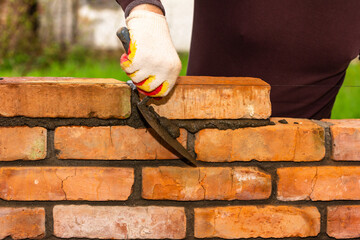 a man's hand with a construction trowel removes excess cement mortar from the brickwork during the construction of the wall