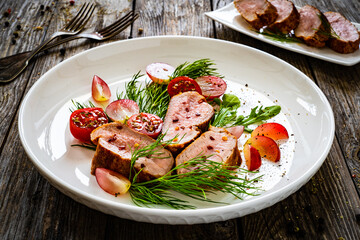 Roasted pork loin slices with dill and cherry tomatoes on wooden table