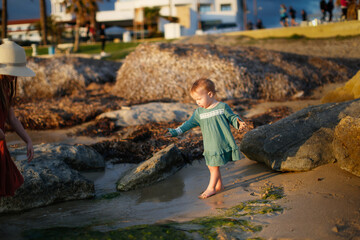 Girl baby toddler in a dress plays on the seashore sunset, lifestyle
