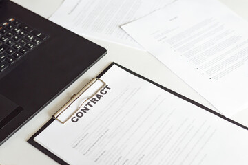 Side view of contract in clipboard lying at office on table with laptop and documents