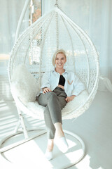 Sitting on a cocoon chair in a bright room. The concept of satisfaction, joy to life. Cheerful girl...