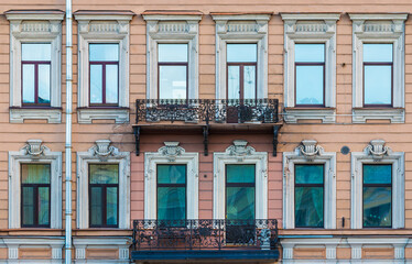 Two balconies and many windows in a row on the facade of the urban historic apartment building...