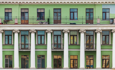 Balconies, columns and many windows in a row on the facade of the urban historic apartment building front view, Saint Petersburg, Russia
