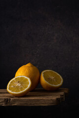 whole and halves of a fresh ripe lemon lie in a group on an old plank table against a dark soft background. side view. moody vertical artistic photo with copy space