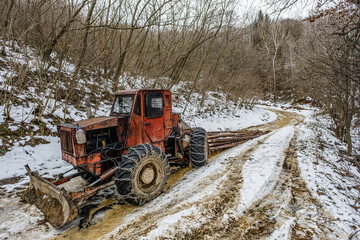 Harvester tractor snowy with wood trunks outside in forest.