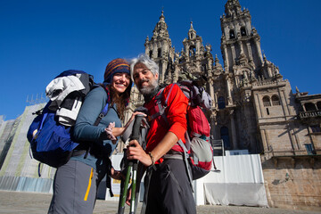 A couple of pilgrims celebrate in front of the cathedral of Santiago that they have reached the end of the journey after walking the Camino de Santiago - obrazy, fototapety, plakaty