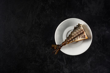 a half-eaten fish tail lies on a white plate on a black concrete background. top view. creative food mockup with copy space