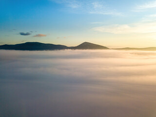 The rays of dawn over the fog in the Ukrainian Carpathians. Aerial drone view.