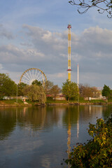 Spring festival (Fr&uuml;hlingsfest) with funny rides. Ferris wheel and free fall tower by the river at evening. Germany, Stuttgart, Wasen.