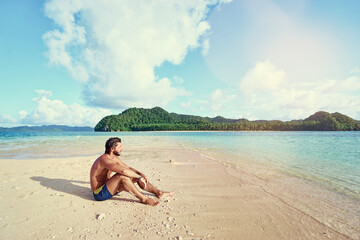 Tropical vacation. Relaxed young man sitting on the sand beach enjoying the island view.