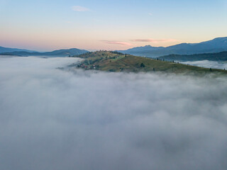 Flight over fog in Ukrainian Carpathians in summer. Mountains on the horizon. A thick layer of fog covers the mountains with a continuous carpet. Aerial drone view.