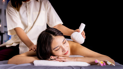 Healthy Asian woman lying in bed doing spa treatment on her back. was compressed with herbs wrapped in a white cloth massage her back to relax There were flowers and candles on the bed.