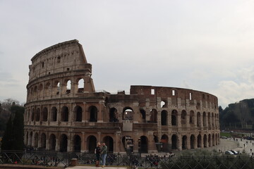 Fototapeta premium ROME, ITALY - February 05, 2022: Panoramic view around the Colosseum in city of Rome, Italy. Cold and gray sky in the background. Macro photography of the green parks with the old buildings.