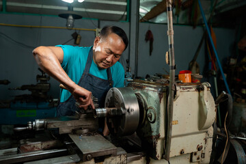 Portrait of a senior Asian man who is a steelworker. using a small steel turning tool to prepare for a lathe job in my family's small lathe.