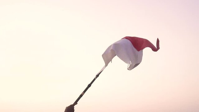 Red and white indonesian flag flying over the hill with golden sky when the sun rises by a group of men