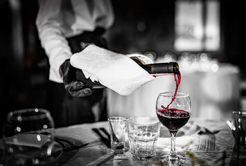 waiter pouring red wine into a glass on table in cafe or restaurant