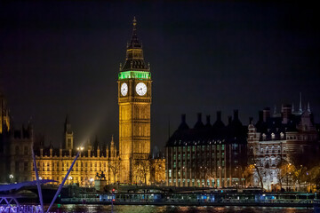 The clock of Elizabeth Tower (Big ben) illuminated in white and green alongside the Palace of...