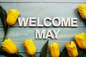 Welcome May alphabet with yellow tulip flower on wooden background