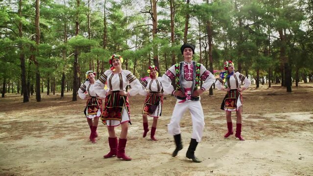 Four young women and one man in traditional costumes are dancing Ukrainian national dances