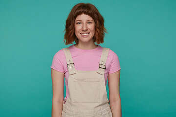 indoor portrait of young ginger female posing over blue background looking into camera with brad...