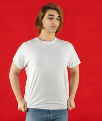 White t-shirt for mock-up print design. A young man wears a short-sleeved t-shirt, jeans, studio shot on a red background. Guy in white clothes for advertising