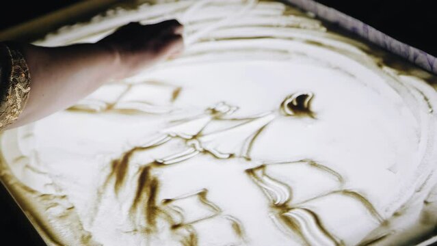 The girl draws a picture with sand. Close-up of the artist's hands
