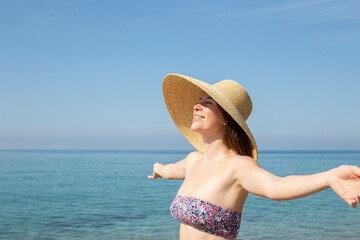 Portrait of a fit young woman wearing bright bikini swimsuit with flower patterns and broad brim straw hat sunbathing at the beach, enjoying ocean view. Background, close up, copy space