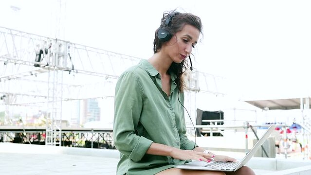 Technical support manager chat with a client. 
Installation of stage equipment and preparing for a live concert open air. Summer music city festival. Woman work with laptop.