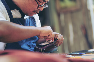 An experienced tanner sews a clasp for a leather product with stitches.