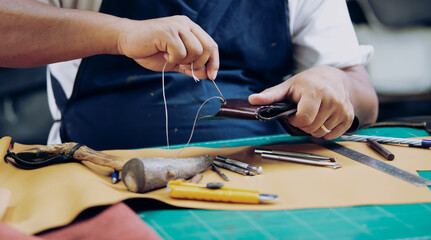 An experienced tanner sews a clasp for a leather product with stitches.