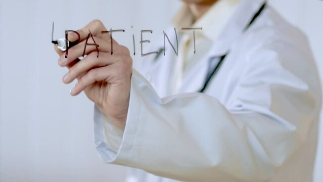 A young unrecognizable caucasian doctor in a white coat with a stethoscope writes the words patient, doctor, help on the glass door of the hospital. Medicine, healthcare.
