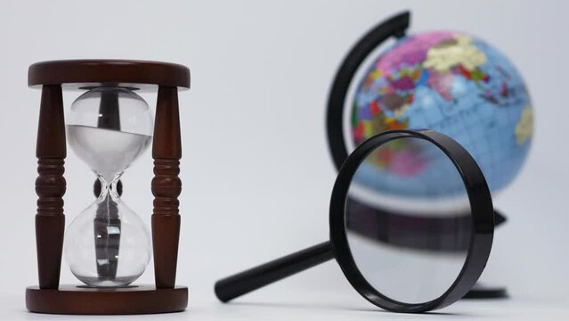 Hourglass, magnifier, globe on white background. Time to travel, discover the world. 4K UHD video.