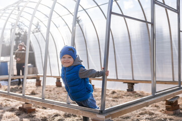 charming boy helps to build a greenhouse. Spring seasonal work. Little Helper