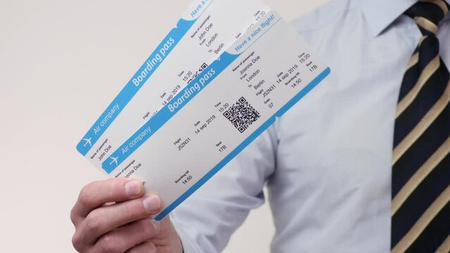 Businessman in white shirt with striped necktie holds two boarding passes or plane tickets, concept of business trip