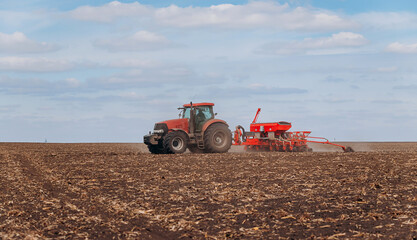 Obraz premium Spring sowing season. Farmer with a tractor sows corn seeds on his field. Planting corn with trailed planter. Farming seeding. The concept of agriculture and agricultural machinery.