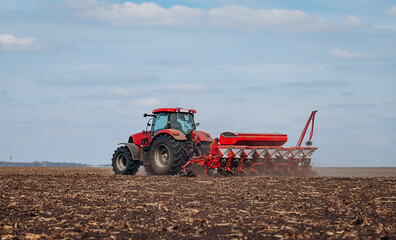 Spring sowing season. Farmer with a tractor sows corn seeds on his field. Planting corn with trailed planter. Farming seeding. The concept of agriculture and agricultural machinery.