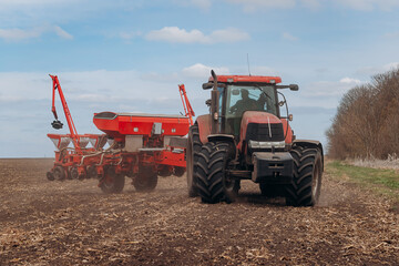 Spring sowing season. Farmer with a tractor sows corn seeds on his field. Planting corn with trailed planter. Farming seeding. The concept of agriculture and agricultural machinery.